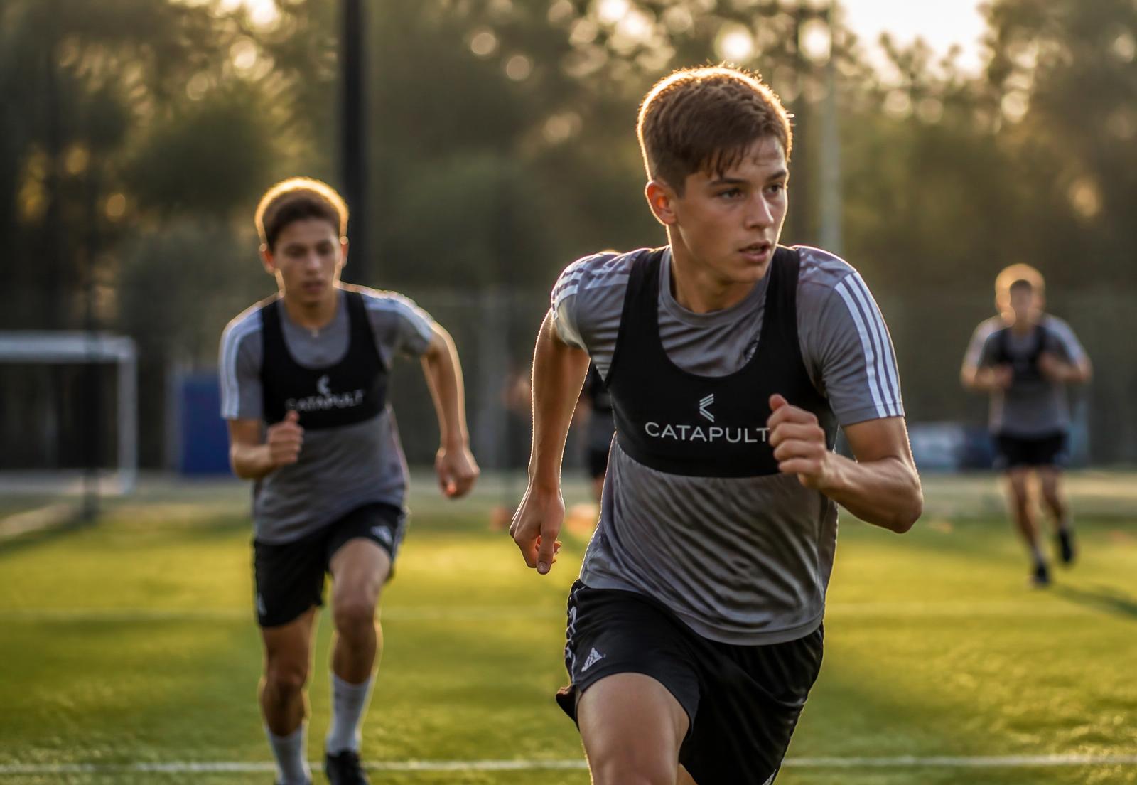 Young footballers sprinting in training while wearing black GPS performance vests